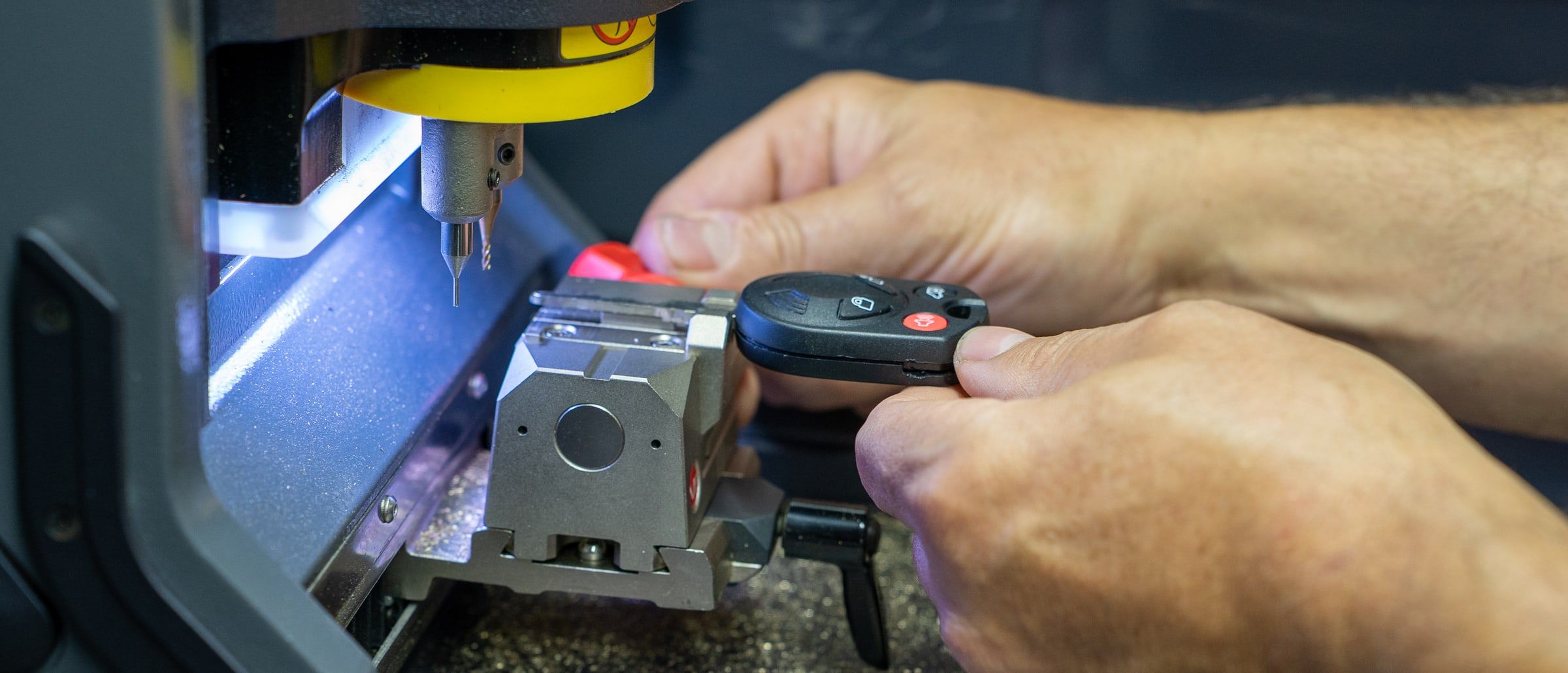 A car key clamped in a key-cutting machine while it is cut, with brass shavings on the bed below.